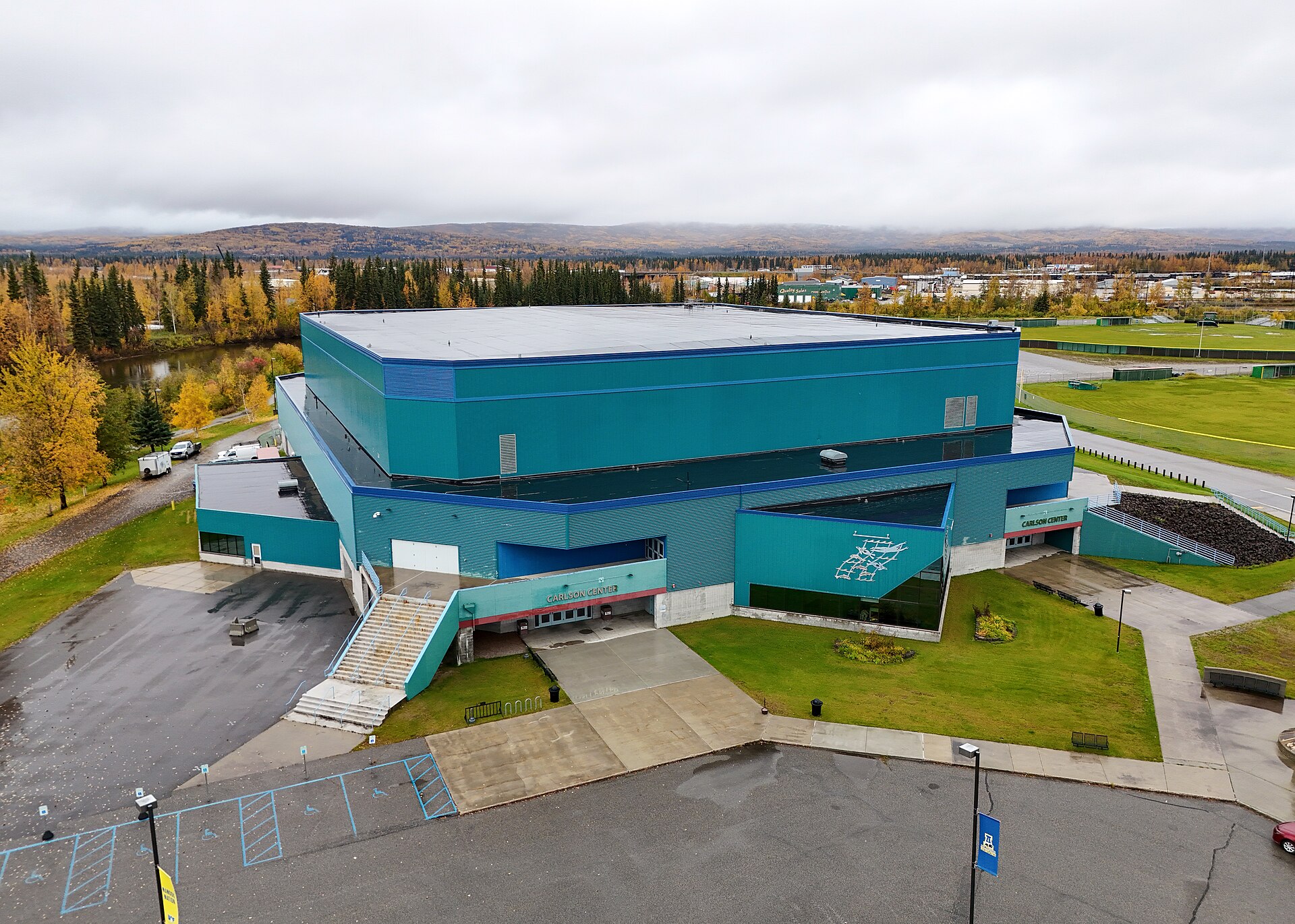 Aerial photo of the Carlson Center in Fairbanks, Alaska, home of UAF Nanooks hockey, with fall trees and hills behind the arena
