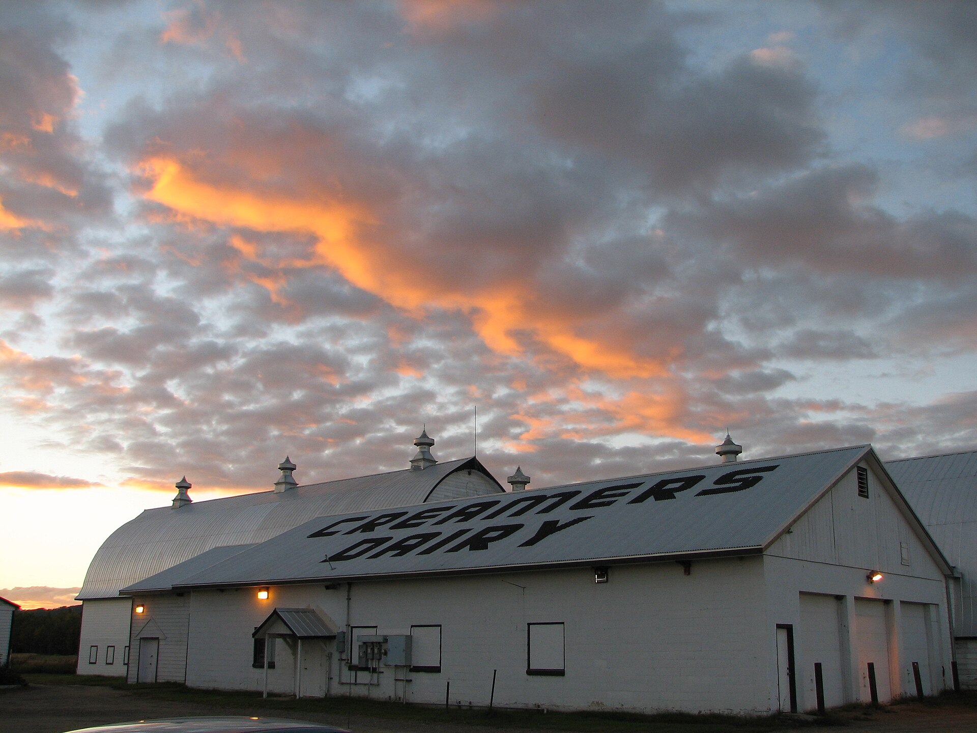 Photo of the white Creamer's Dairy barn at Creamer's Field in Fairbanks, Alaska, under orange sunset clouds