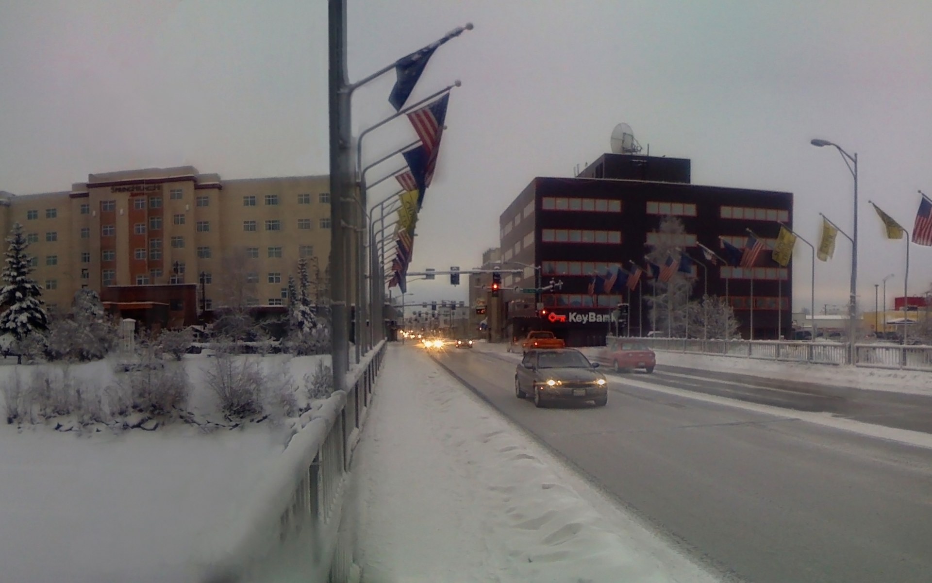 Photo of a snowy Cushman Street bridge into downtown Fairbanks, Alaska, in January, with cars, flags, and frosted trees along the road